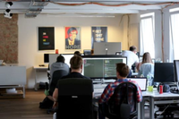 People sit in the back of the office at several tables in a row, both in pairs and alone, and program.