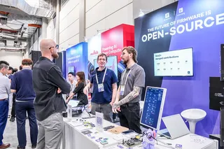 Foto vom OCP APAC Summit 2026 in Taipei vom Stand von 9elements und canopy, eine interessierte Person unterhält sich mit 2 9elements Mitarbeitenden.
