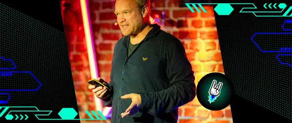Sebastian Deutsch bei seinem Vortrag auf dem DMKR, während er über „Transformational AI“ spricht; er steht vor einer beleuchteten Backsteinwand, spricht engagiert ins Publikum und hält ein Smartphone in der Hand.